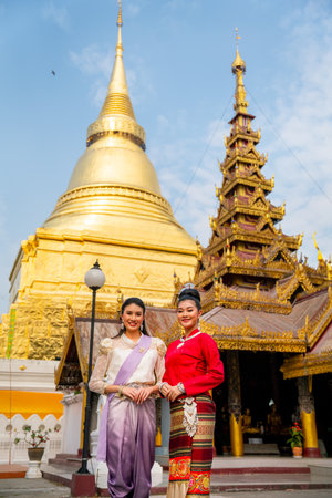 Vertical image of two women stand in front of golden pagoda and ancient building of the temple in Thailand and they also smile to camera.の写真素材
