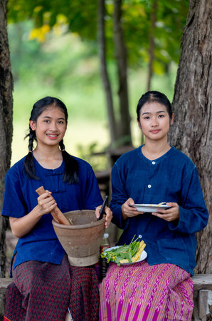 Portrait of two Asian girls hold plate and motar and look at camera with smiling and they sit under the big tree with day light.の写真素材