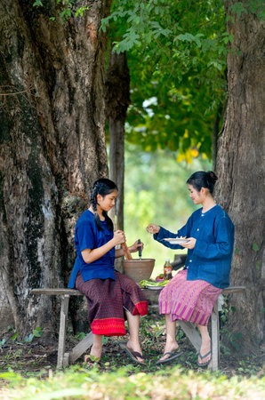 Asian girl with traditional farmer cloth help to cook with her friend by pour pieces of papaya to motar for making papaya salad.の写真素材