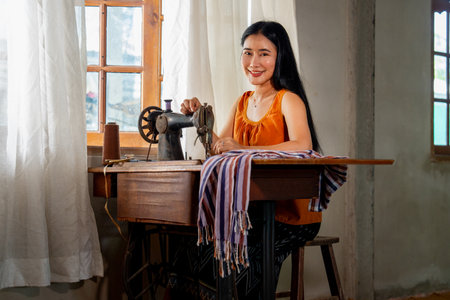 Portrait of beautiful Asian woman with traditional cloth and sit near old sewing machine and look at camera with smiling.の写真素材