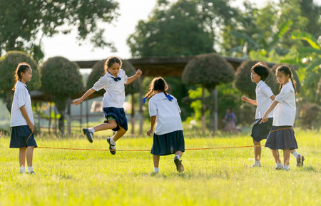 Group of Asian girls wear student uniform enjoy to play with jump across rubber string in grass field area of school.の写真素材