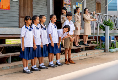 Group of Asian student with uniform stand in a row in front of building and some girl action of poke her friend and teacher in the back also see about the action.の写真素材