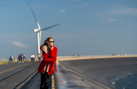 Beautiful Caucasian waman with sunglasses stand in front of wind turbine or windmill also look to right side near the road with smiling of happiness.の写真素材