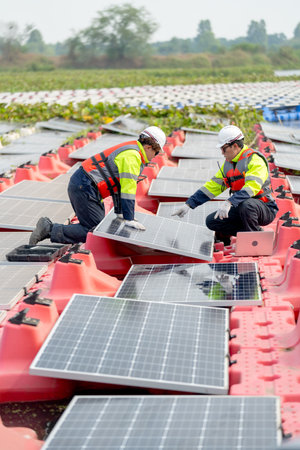 Vertical image of professional technician worker use laptop to work with other co-worker touch to check and maintenance solar cell panel in workplace over water reservoir.の写真素材