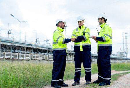 Three engineer or technician workers stand on the road near petrochemical factory and use tablet to discuss their work.の写真素材