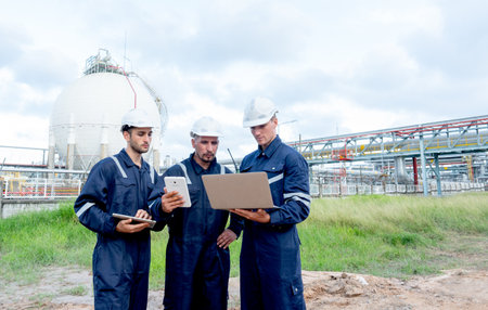 Group of engineer or technician workers stand and look to laptop in front of petrochemical factory with cloudy sky.の写真素材