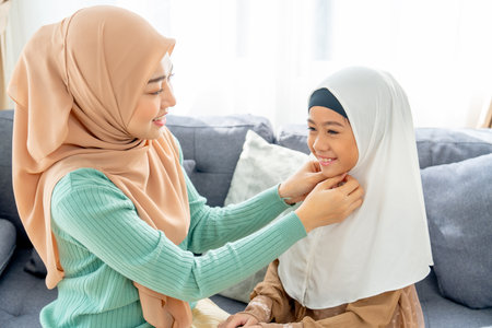 Close up Asian muslim mother help her daughter to wear headscarf or hijab for her and stay in living room of their house with day light and happiness.の写真素材
