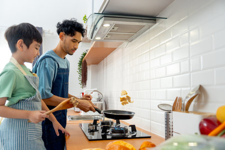 Young Asian father show skill of cooking by throwing pan cake up and his son cheer up beside in the kitchen of their house.の写真素材
