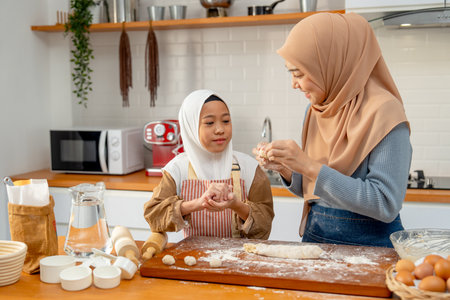 Side view of Asian muslim mother teach her daughter to threshing flour to be like ball shape for making bakery together in kitchen of their house.の写真素材