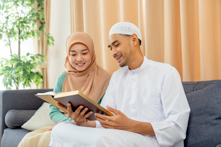 Couple muslim man and woman sit on sofa and read islam teaching book together and they smile with happiness.の写真素材