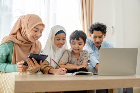 Little Asian muslim girl use pencil to write on notebook to play with her younger brother and father and mother work and sit beside them in their house.の写真素材
