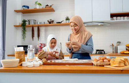 Wide shot of Asian muslim mother teach her daughter to threshing flour to be like ball shape for making bakery together in kitchen of their house.の写真素材