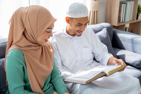 High view of couple muslim man and woman sit on sofa and read islam teaching book together and stay in living room of their house.の写真素材