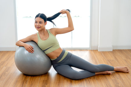Close up Beautiful Asian woman with exercise clothes lie on exercise grey ball with use right hand lean to ball  and use left hand hold her hair and look at camera with day light in front of window.の写真素材