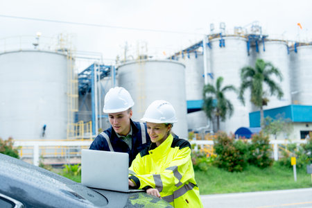 Two technician of engineer workers of petrochemical factory use laptop on back of car and dicussion together with happiness.の写真素材