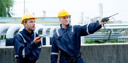 Two petrochemical or gas factory worker men discuss about work with one point to their left side and stand in front of pipeline of factory.の写真素材
