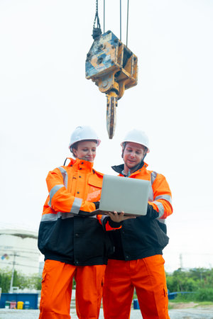 Vertical image of two factory workers or engineer man and woman work near crane in front of factory in the workplace.の写真素材