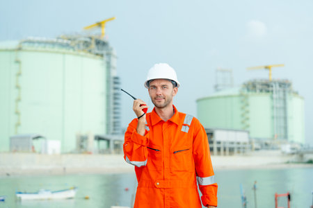 Petrochemical or gas factory worker talk with walkie talkie and look at camera and stand in front of tank in factory.の写真素材