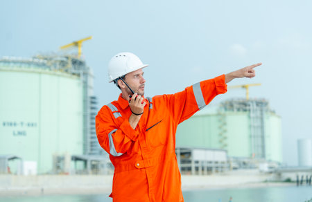 Petrochemical or gas factory worker talk with walkie talkie and point to his left side in front of tank in factory.の写真素材