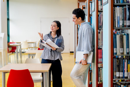 Close up shot Hispanic man lean against side of bookshelf and discuss with Asian woman about the detail in some books in public library.の写真素材