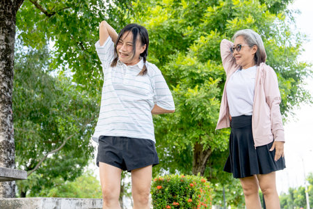 Asian senior woman stand and guide to her friend to stretching arm and shoulder in the garden wiith day light.の写真素材