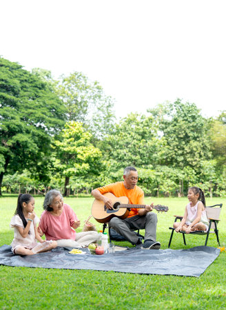 Vertical image of Asian senior man play the guitar while senior woman and two little girl clap hands...