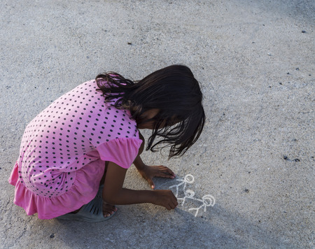 Girl drawing families with parents and children holding hands happily onto a concrete floor.の写真素材