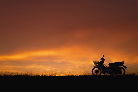 Orange sunset sky. Silhouette motorcycle in sunset landscape backdropの写真素材