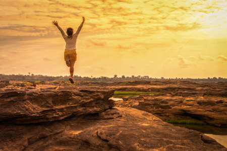 Young woman jumping hands up relaxing in sunset sky landscape outdoorの写真素材