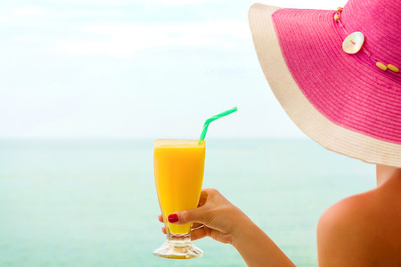 Young female, drinking orange juice, on the beach 