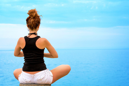 Young woman doing yoga, looking at ocean horizon の写真素材