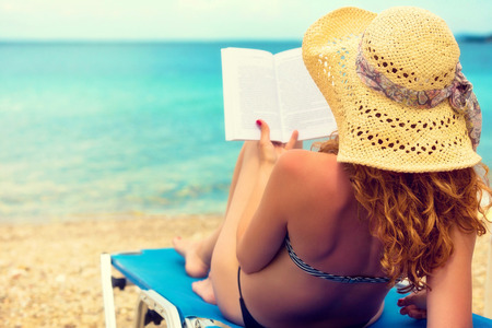 Curly hair female reading a book on the beach の写真素材