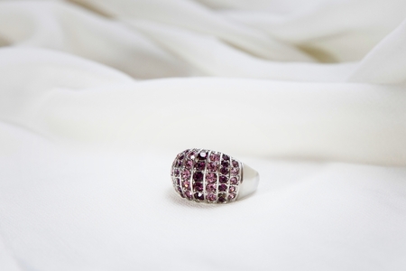 Silver ring with pink and lilac zircons, on white silk.の写真素材