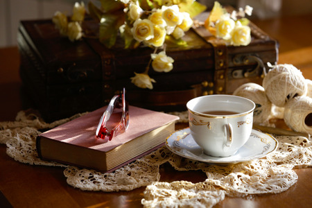 Romantic composition of tea cup, closed book and glasses, on crochet lace.の写真素材