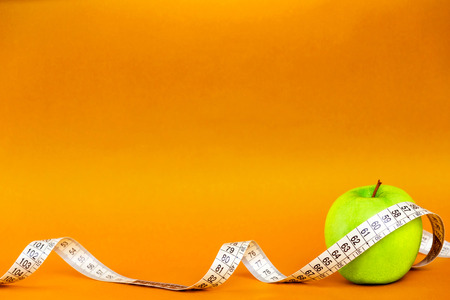 Green apple with tape measure isolated on orange background.の写真素材