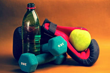 Composition presenting healthy lifestyle,with green apple,boxing gloves,bottle of water and dumbbells,against orange background.の写真素材