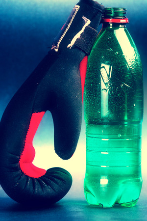 Green bottle of water and black boxing glove,against blue background.の写真素材