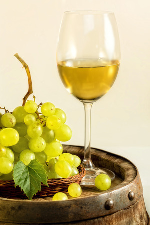 Glass of white wine and green grapes on old barrel, in light cellar.の写真素材