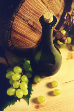 Bottle of wine, green grapes and old barrel, placed on wooden table, in light cellar- top view.の写真素材