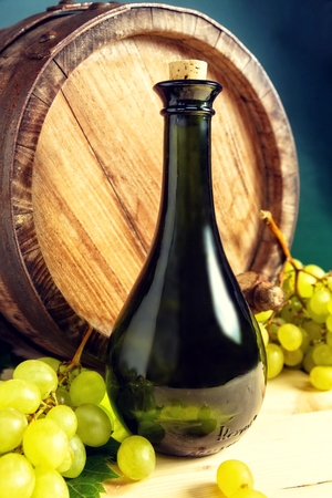 Bottle of wine in front of wine barrel with white grapes.の写真素材