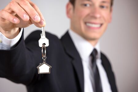 Young businessman giving house keys, isolated on grey background.の写真素材