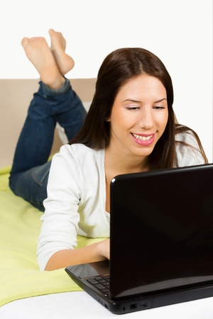 Cute young woman, surfing the internet, lying on her bed.の写真素材