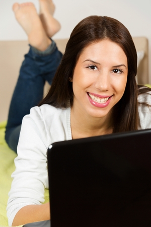 Cute teenage girl, surfing the internet, lying on her bed.の写真素材