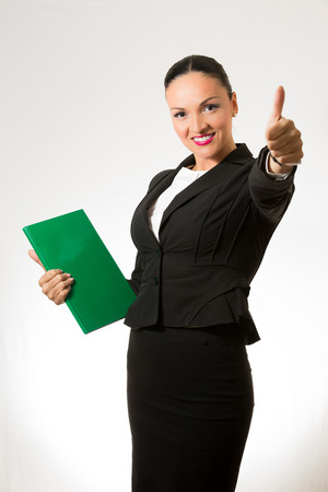 Black hair business dressed woman holding green book and hand up.の写真素材