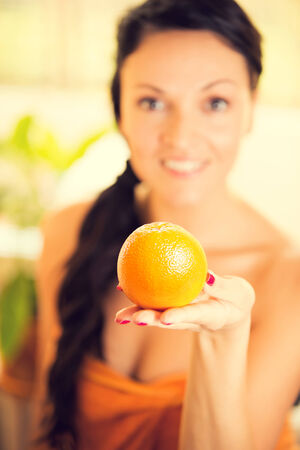 Beautiful young woman holding an orange fruit and smiling.の写真素材