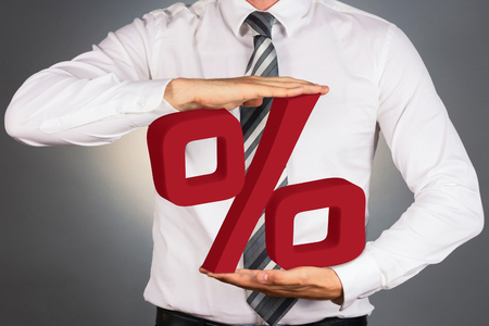 Adult businessman holding 3 D percent sign isolated on dark background.の写真素材