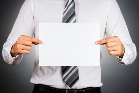 Business man holding a blank white board isolated on dark gray background.の写真素材