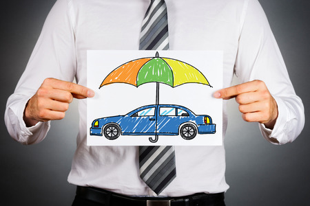 Car insurance concept. Businessman holding withe paper with drawn colorful car under safety umbrella.の写真素材