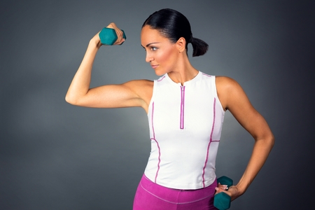 Professional sporty muscular model working out with two dumbbells, isolated on dark background.の写真素材