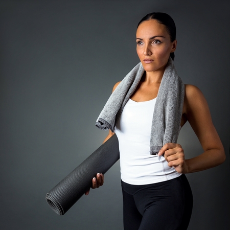 Beautiful fitness woman posing with yoga mat, isolated on dark grey background.の写真素材